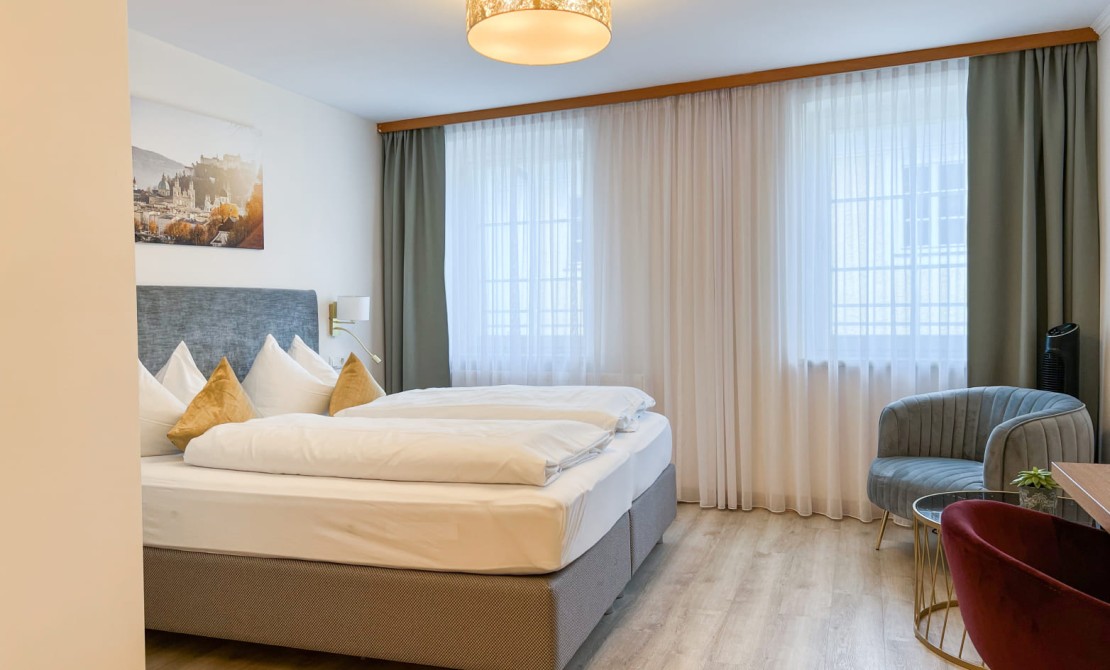 Dreibettzimmer in der Trumer Stube Salzburg mit komfortablem Doppelbett und Sitzecke