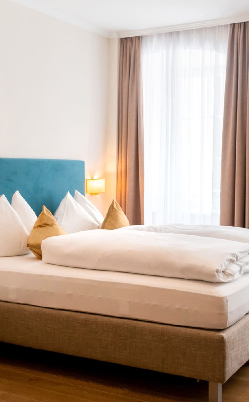 Gem&uuml;tliches Doppelbett mit stilvollen Kissen und viel Tageslicht im Dreibettzimmer